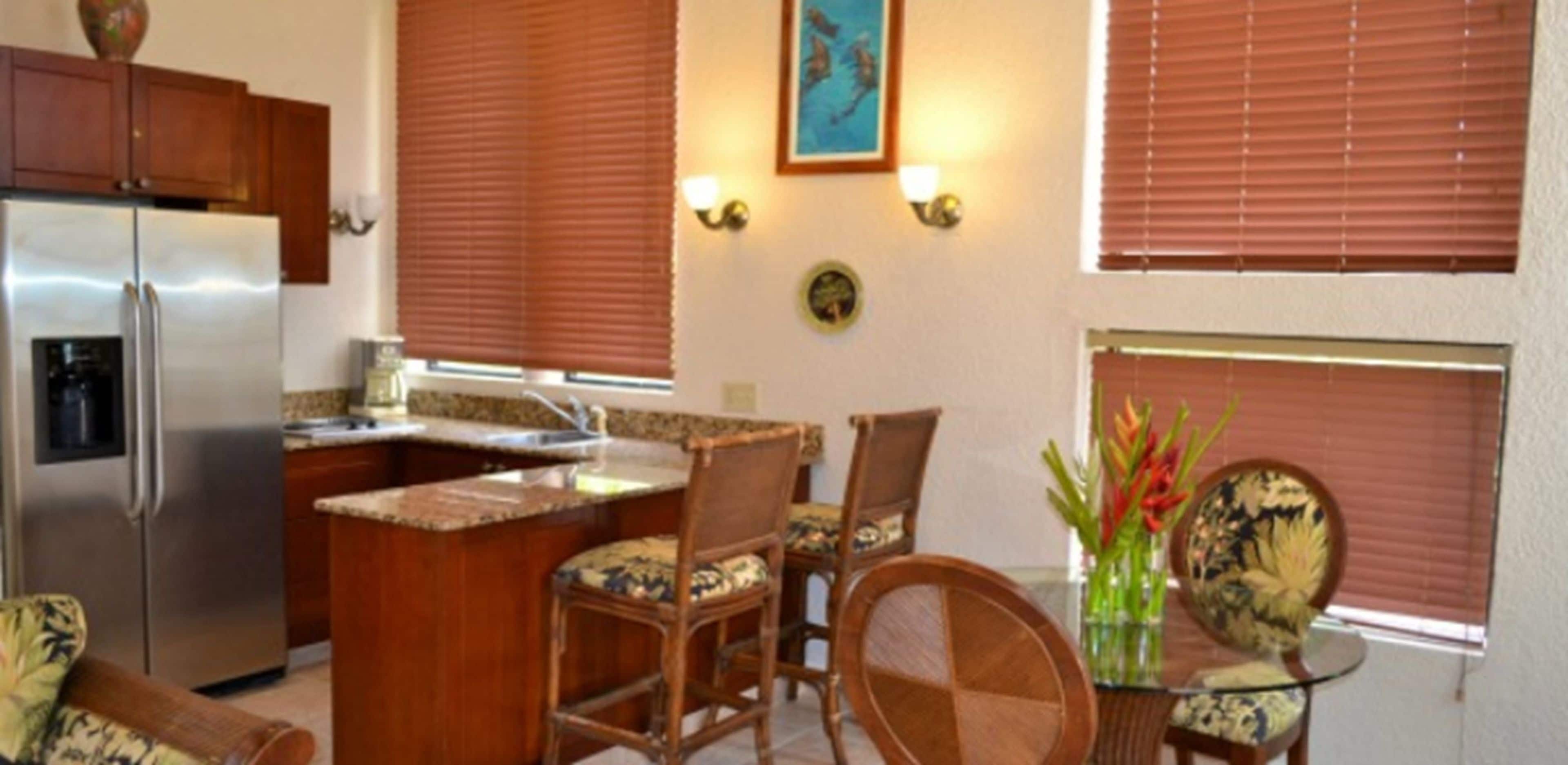 A compact kitchen with a refrigerator, a dining area with chairs and a table, and a window with blinds.