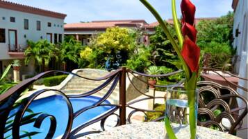 A pool area with a metal fence, a red flower, and a building with a tiled roof in the background.