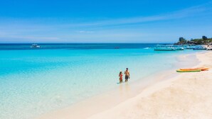 A beach with clear turquoise water, a sandy shore, and a few boats. - Mayan Princess Beach & Dive Resort - All Inclusive (Roatan)