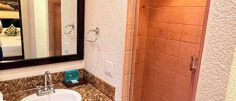 A bathroom with a granite countertop sink, a mirror, and a shower with a glass door.