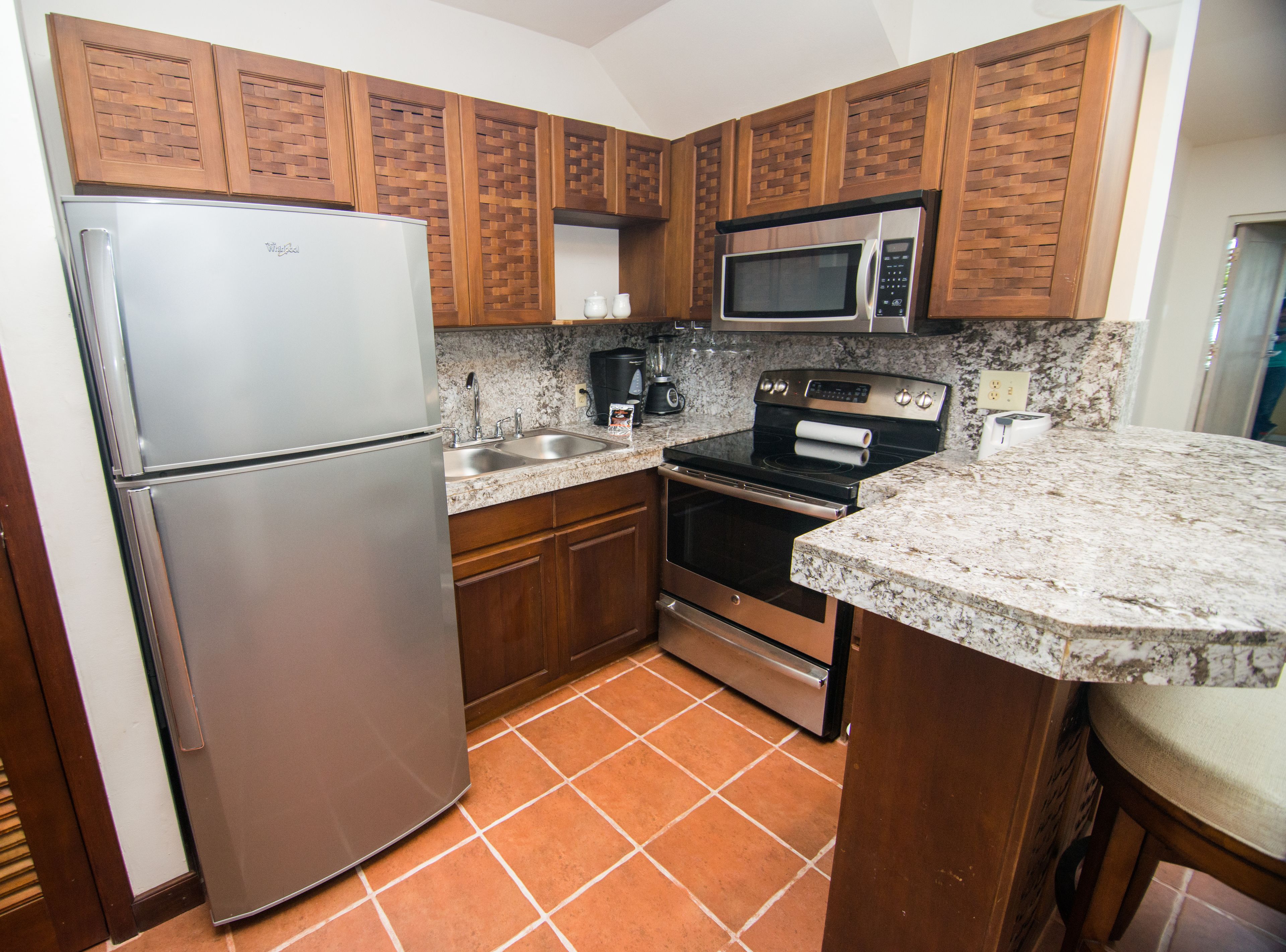 A kitchen with a refrigerator, double sink, microwave, stove, and granite countertop.