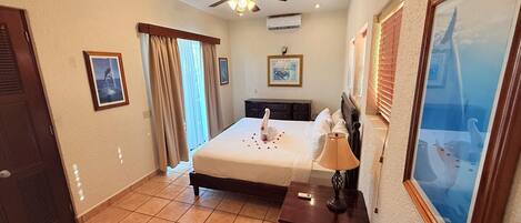 A hotel room with a bed, a nightstand, a ceiling fan, and a large window with blinds.