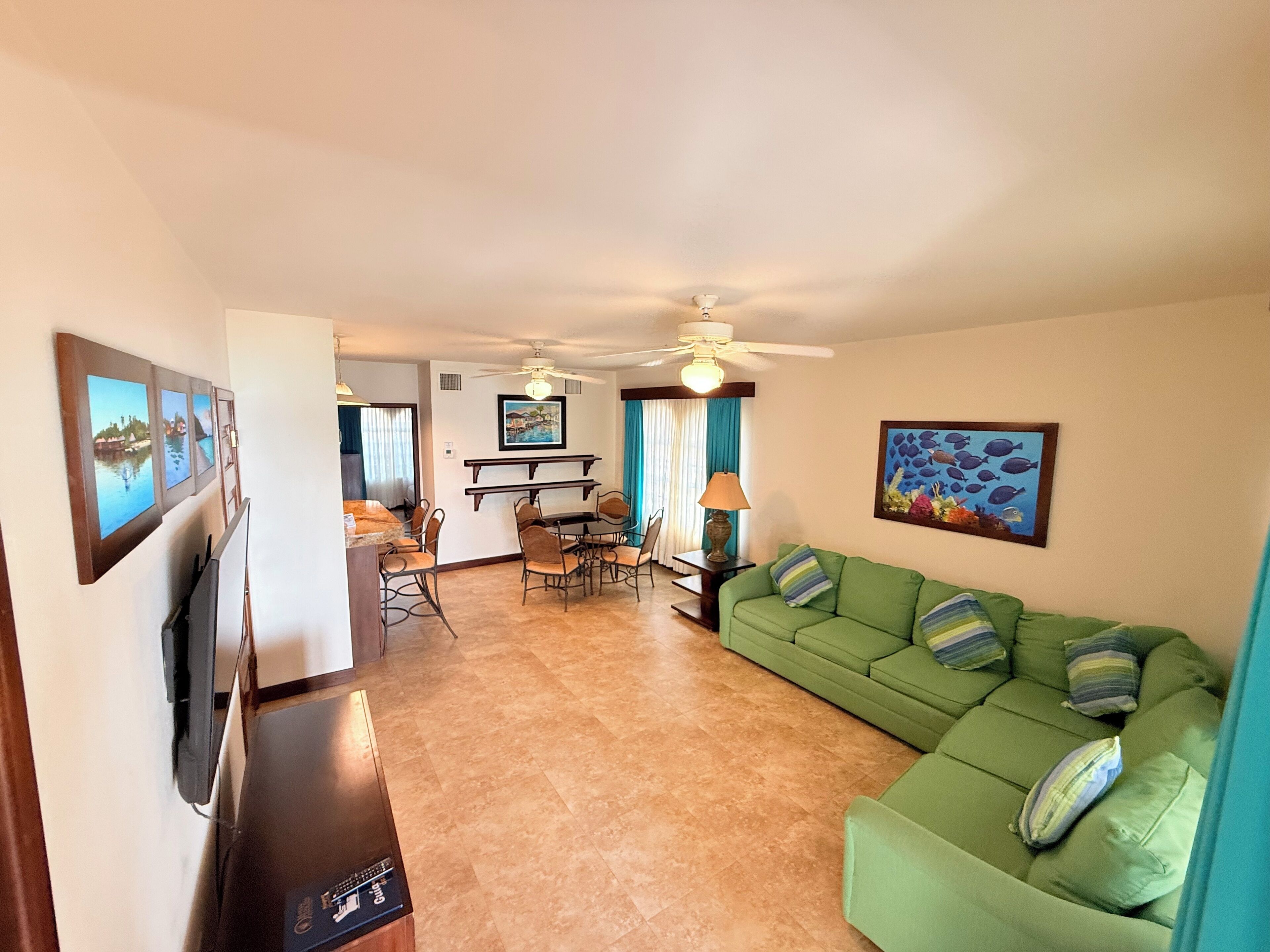 A living room with a green sofa, a dining area with a table and chairs, a ceiling fan, and a TV on a stand.