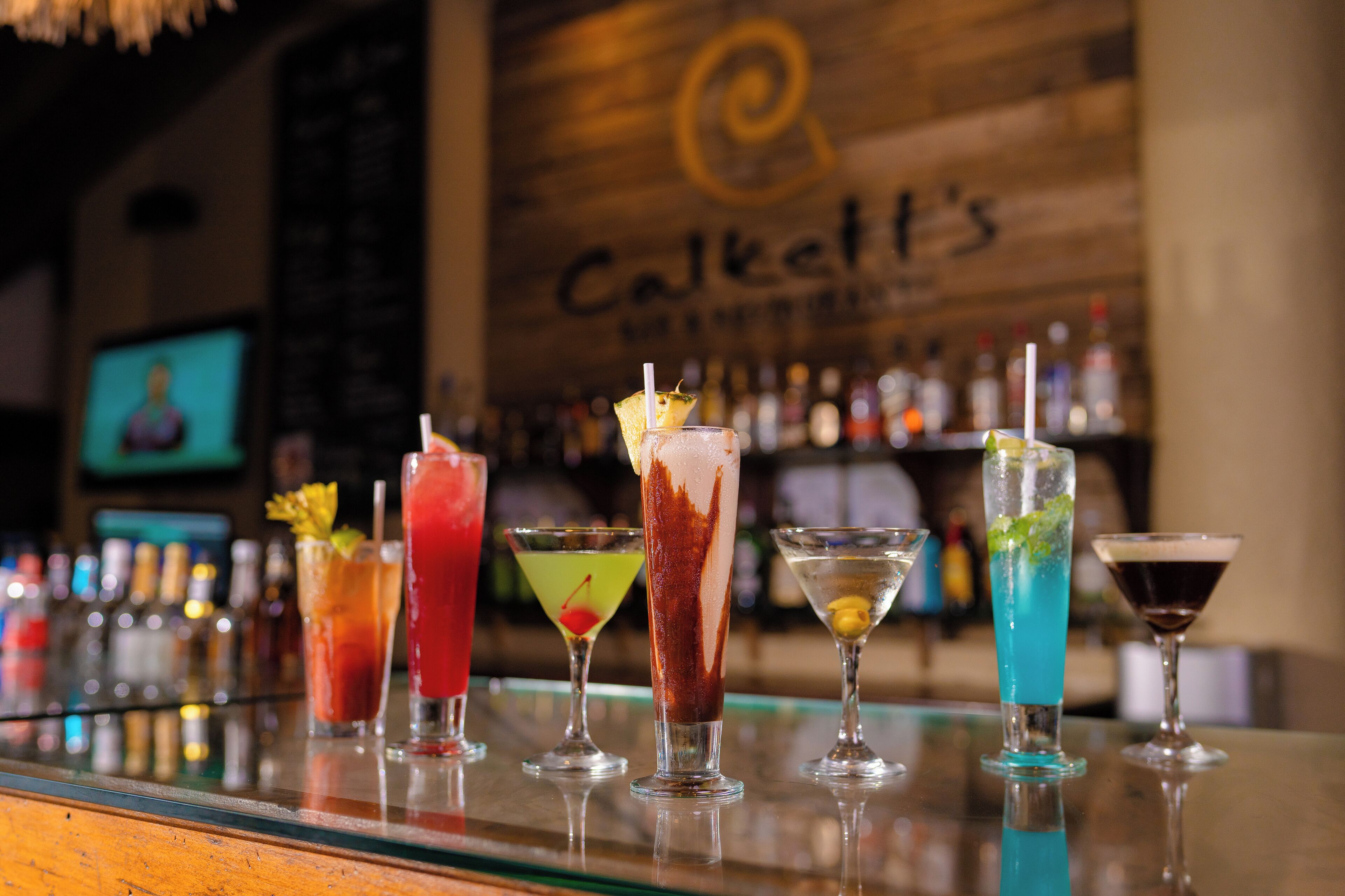 A bar with various cocktails and a wooden wall with the text "Calkett's".