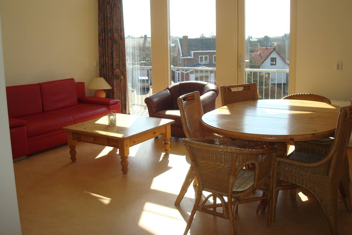 A living room with a red sofa, a wooden coffee table, wicker chairs, and a dining table.