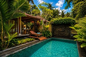 A swimming pool with a wooden deck, lounge chairs, and tropical vegetation. - Segening Villa (Ubud)