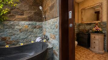 Un baño con pared de piedra, una bañera independiente, un tocador de madera y un espejo.