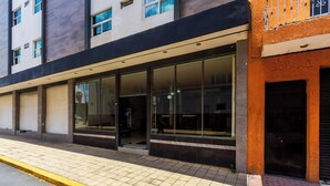 A modern building with large glass windows, a black awning, and a tiled sidewalk. - Capital O Hotel Colón Express Guadalajara (Guadalajara)