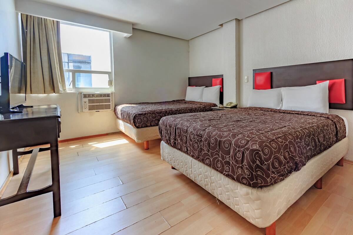 A hotel room with two beds, a desk, and a window with curtains.