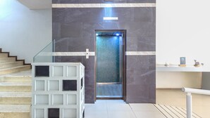 A modern elevator with a glass panel, a staircase with a glass railing, and a clean, tiled floor. - Capital O Hotel Colón Express Guadalajara (Guadalajara)