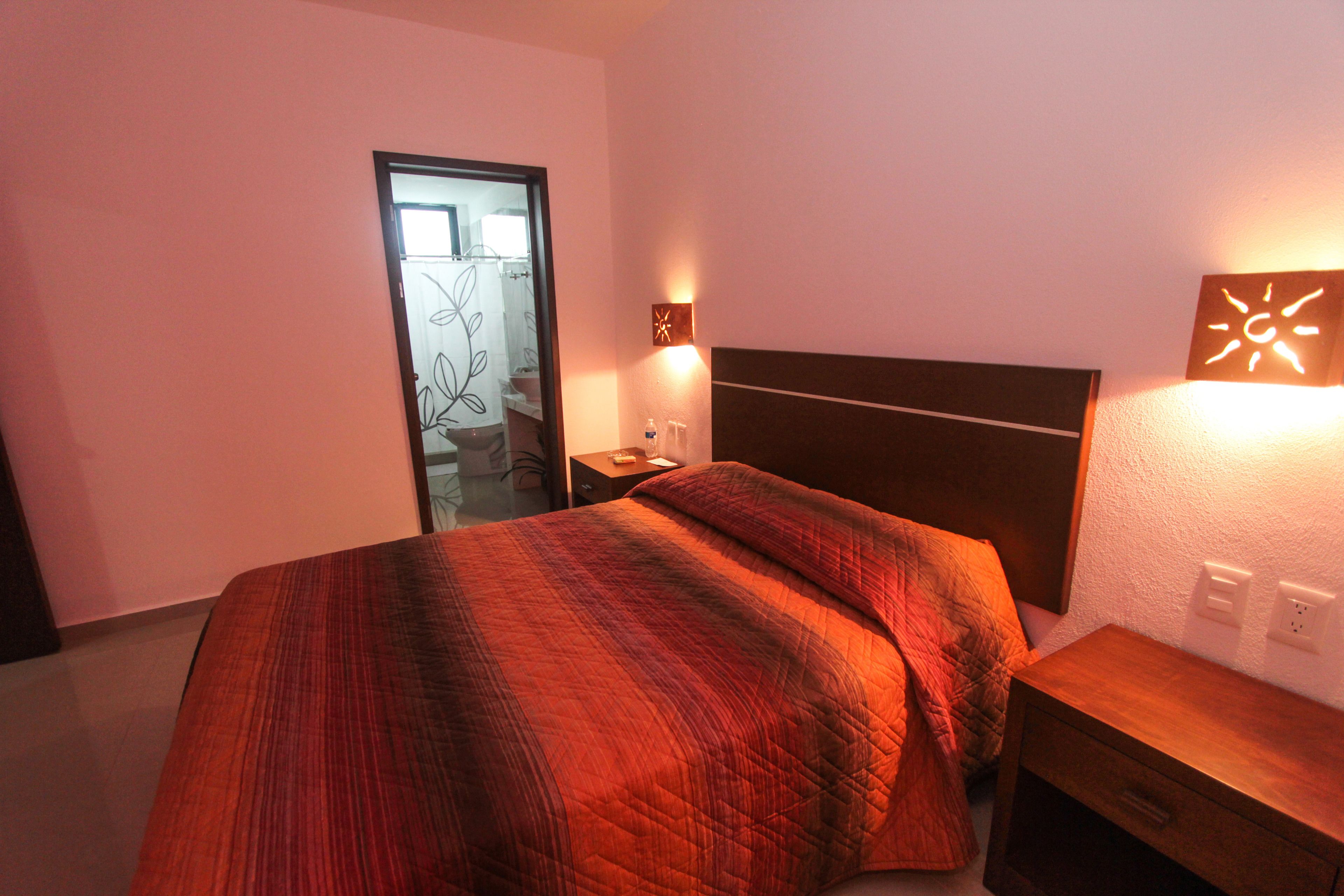 A hotel room with a bed, bedside table, nightstand, and a mirror.