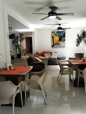 A modern living room with a sofa, dining table, chairs, ceiling fan, and a painting on the wall.