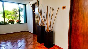 A hallway with tiled flooring, two black vases with sticks, a door with the number 14, and a window with plants outside.