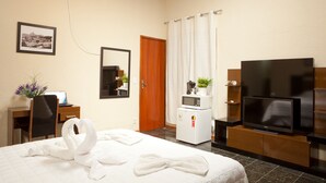 A hotel room with a bed, a desk with a laptop, a microwave, a TV, and a door with a curtain. - HMG Praia Suites for Rent (Rio de Janeiro)