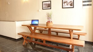A wooden picnic table with a laptop and a vase of flowers on it, set against a wall with two framed pictures. - HMG Praia Suites for Rent (Rio de Janeiro)