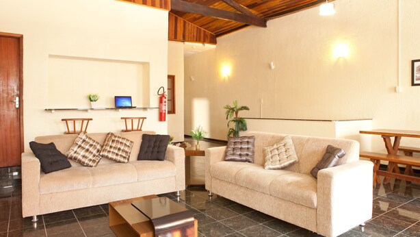 A living room with two beige sofas, a glass coffee table, wooden beams on the ceiling, and a small plant on a shelf. - HMG Praia Suites for Rent (Rio de Janeiro)