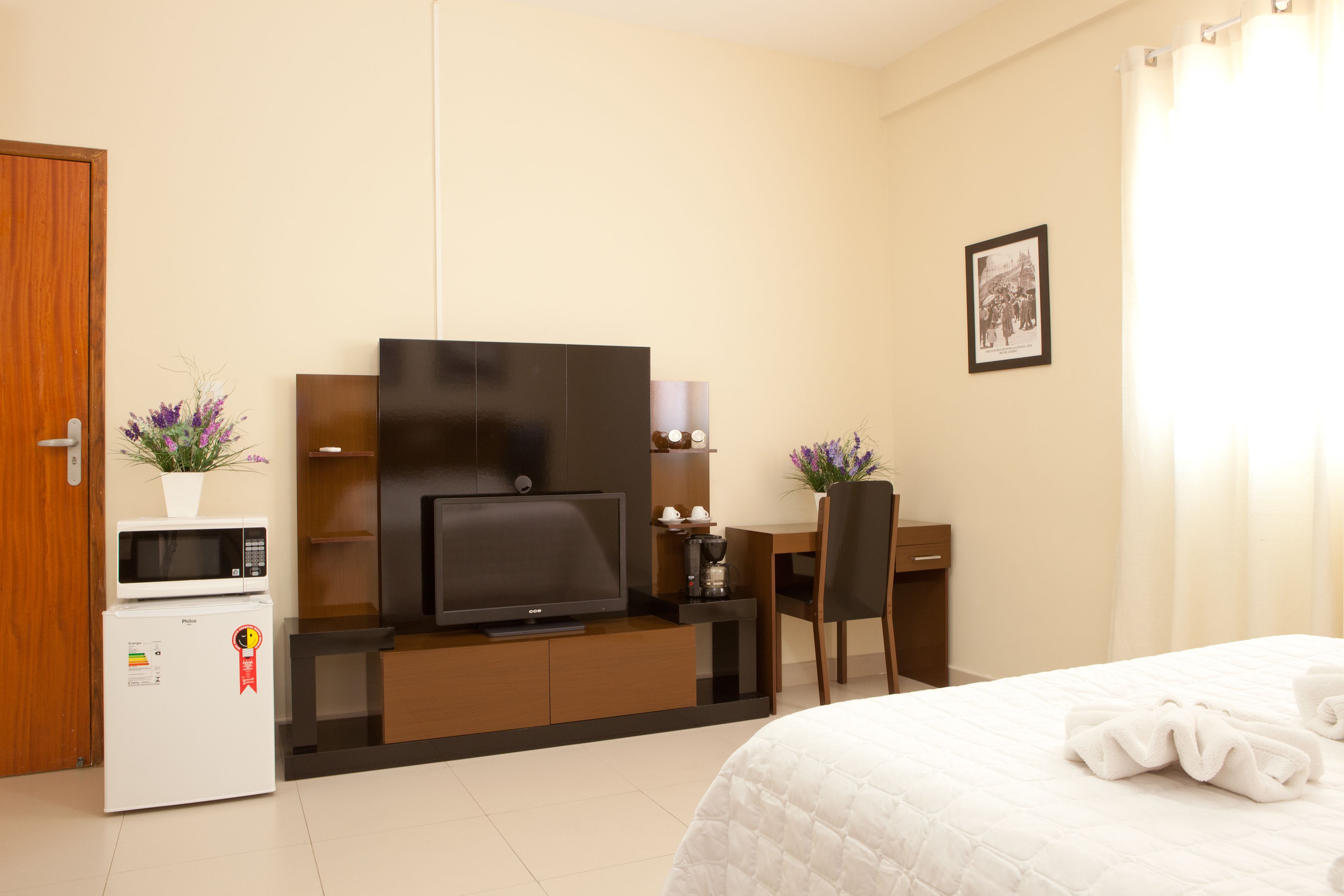 A hotel room with a bed, a TV, a microwave, a coffee maker, and a desk with a chair.