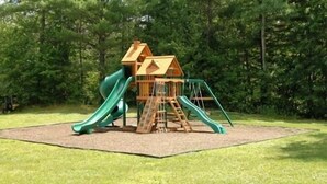 A playground with a slide and climbing structures in a grassy area with trees in the background. - Saco River Motor Lodge & Suites (Center Conway)