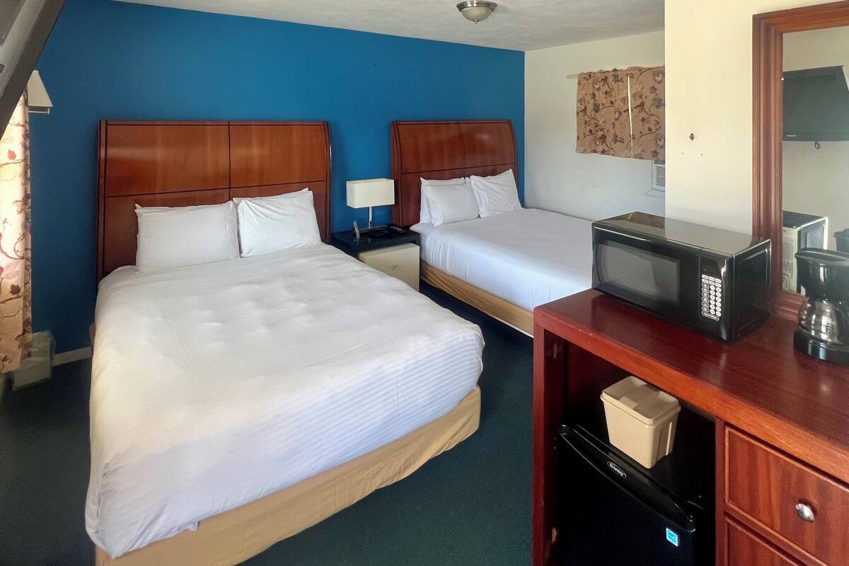 A hotel room with two beds, a desk with a microwave, and a dresser.