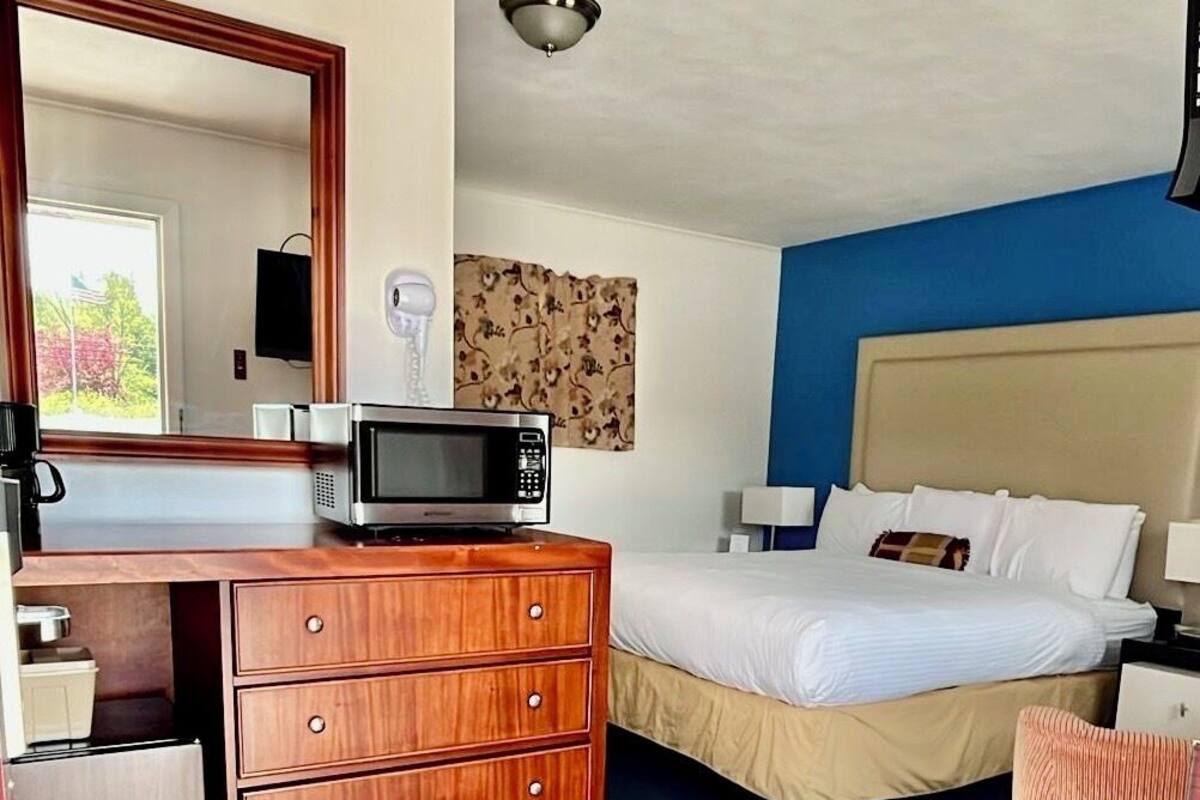 A hotel room with a bed, a dresser, a microwave, a television, and a ceiling light.