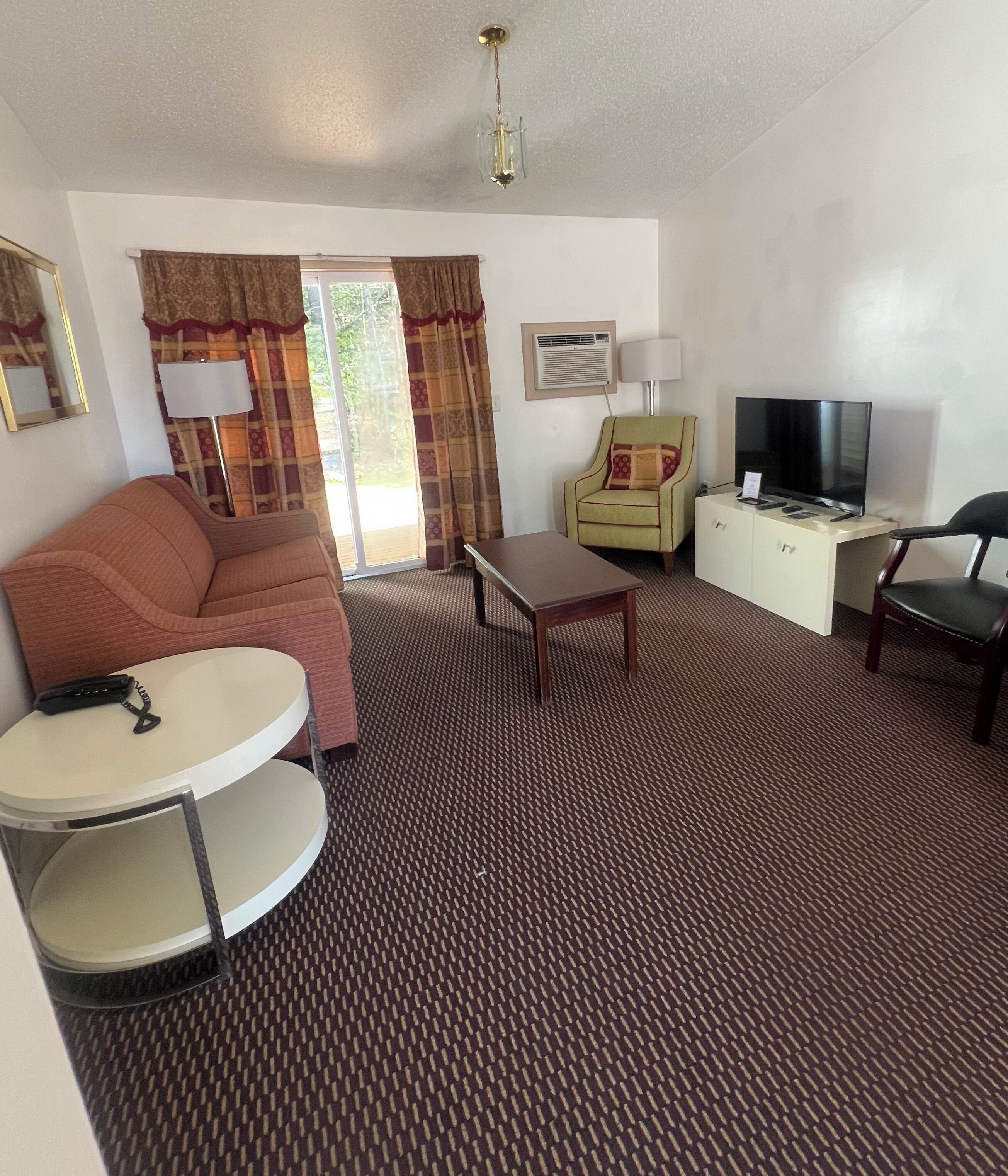A hotel room with a sofa, a small round table, a TV on a cabinet, and a patterned carpet.