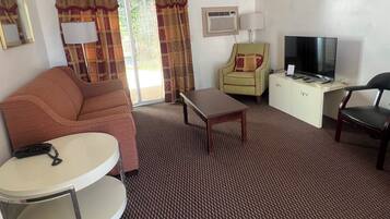 A hotel room with a sofa, a small round table, a TV on a cabinet, and a patterned carpet.
