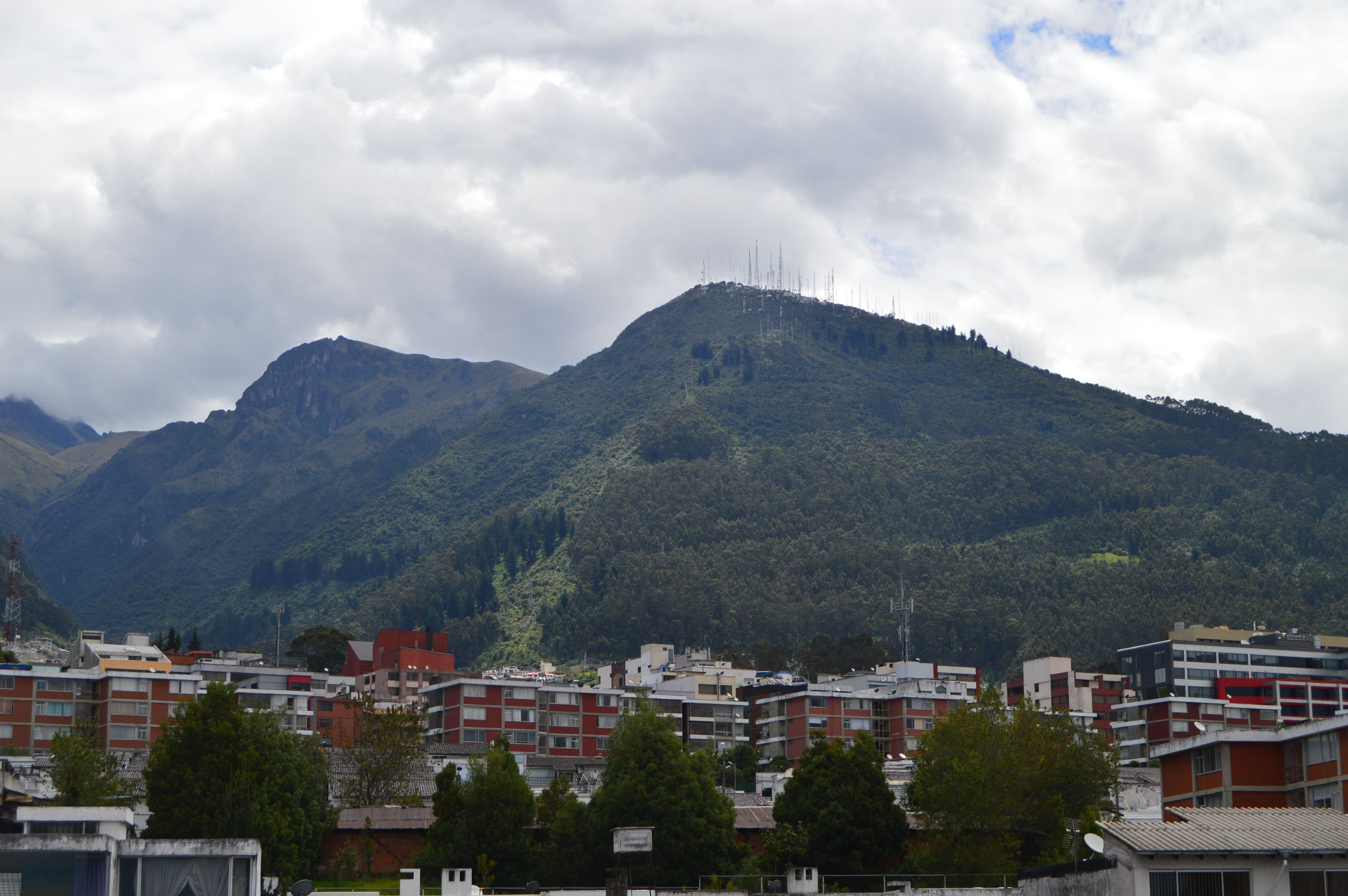 Une montagne couverte d’une forêt dense et, au premier plan, une ville avec des bâtiments aux couleurs rouge et blanche.