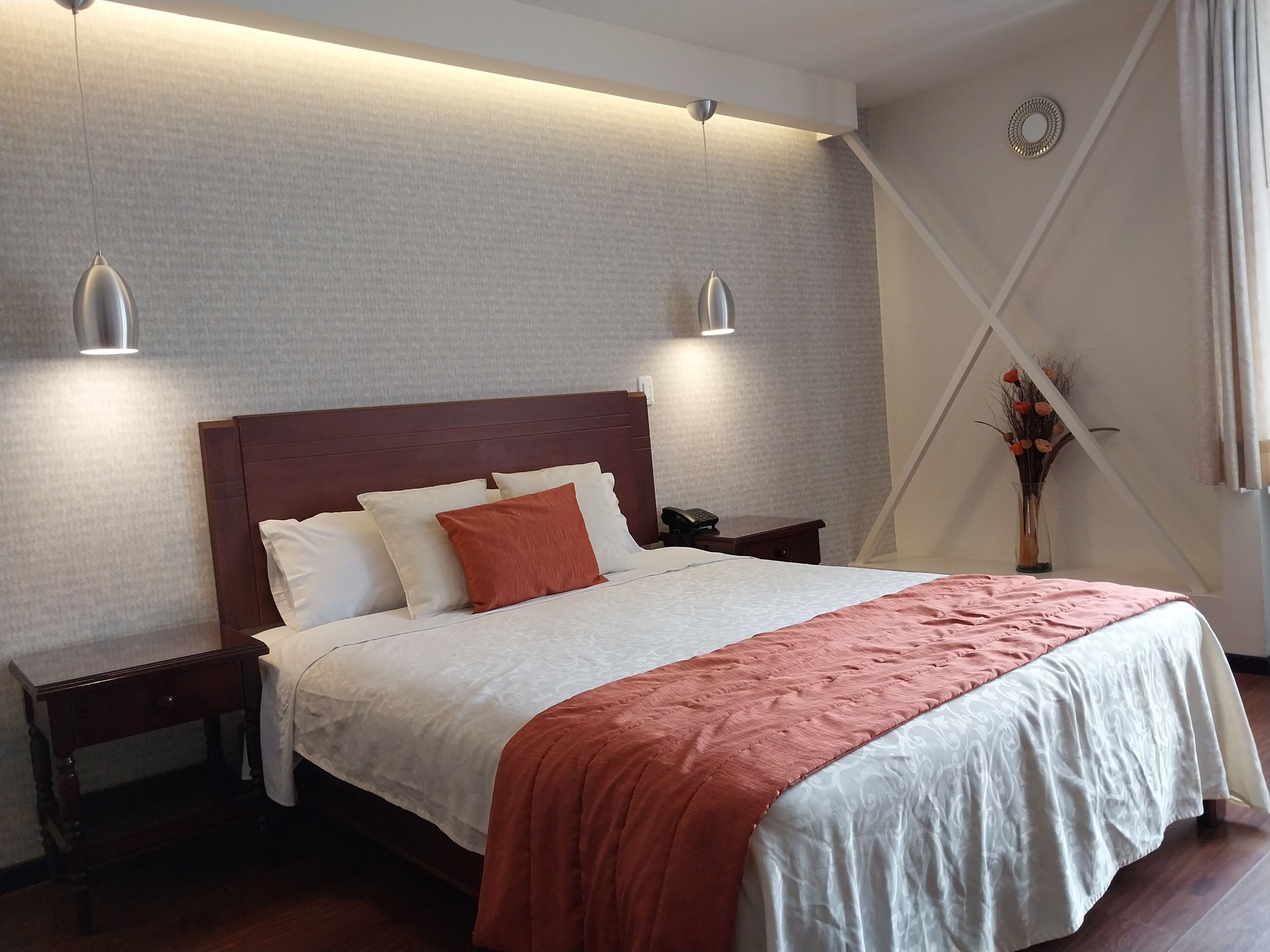 A neatly made bed with a wooden headboard, two bedside tables, and a vase with flowers on the nightstand.