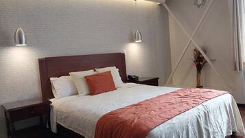 A neatly made bed with a wooden headboard, two bedside tables, and a vase with flowers on the nightstand.