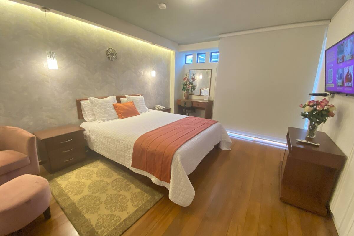 A modern bedroom with a large bed, bedside tables, a desk, and a chair.