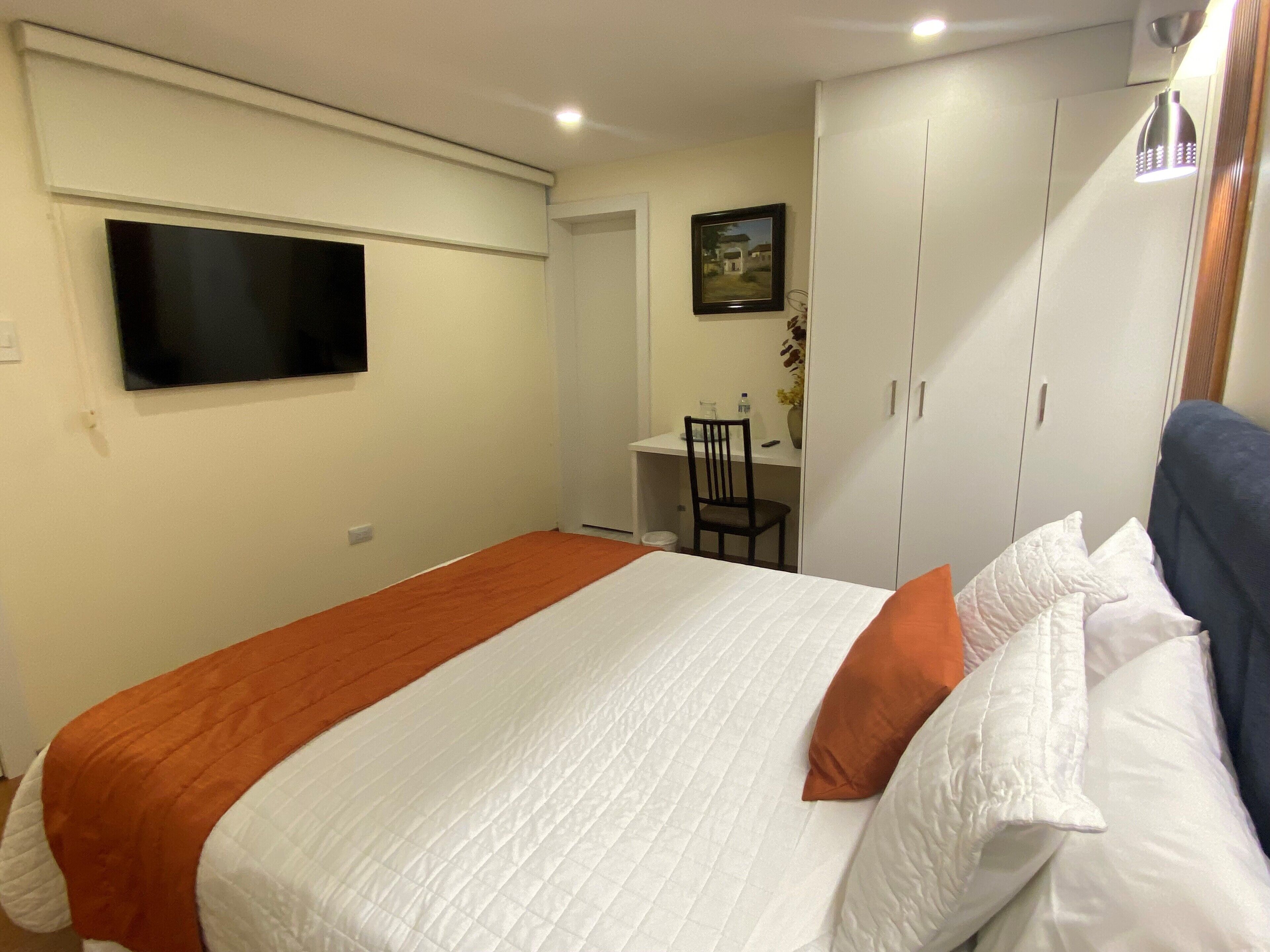 A bedroom with a bed, a desk, and a wardrobe.
