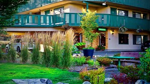 A hotel with a reception area, a balcony with green railings, and a well-maintained garden with various plants and a bench.