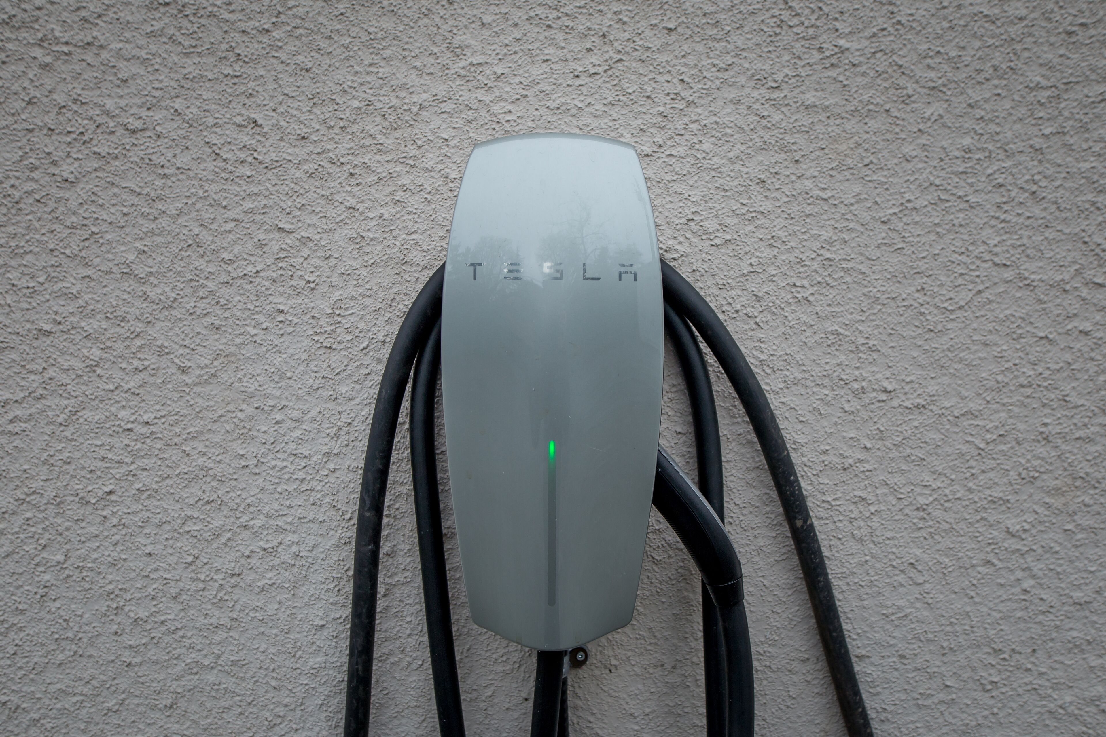 A Tesla charging station with the Tesla logo, connected to multiple cables.