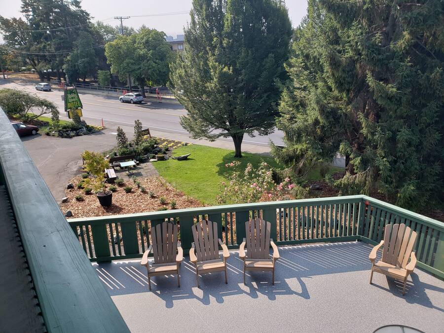 A motel with a green deck, outdoor seating, and a view of the street and trees.