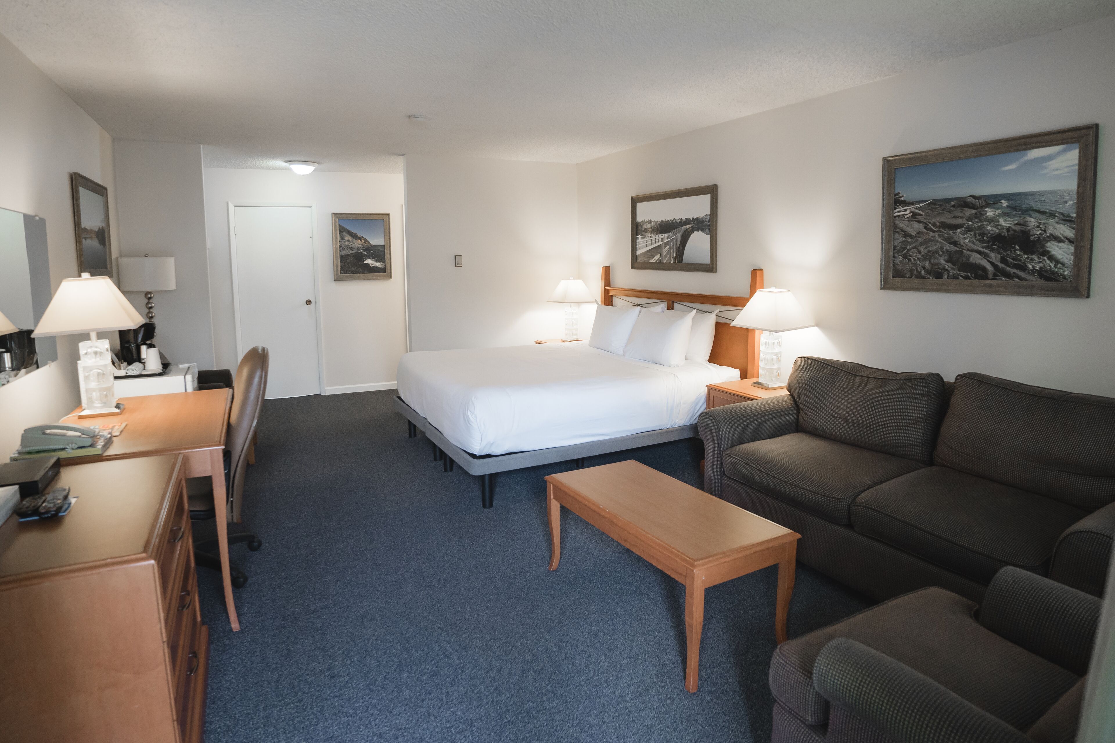 A hotel room with a bed, a desk, a chair, a sofa, and a small table.