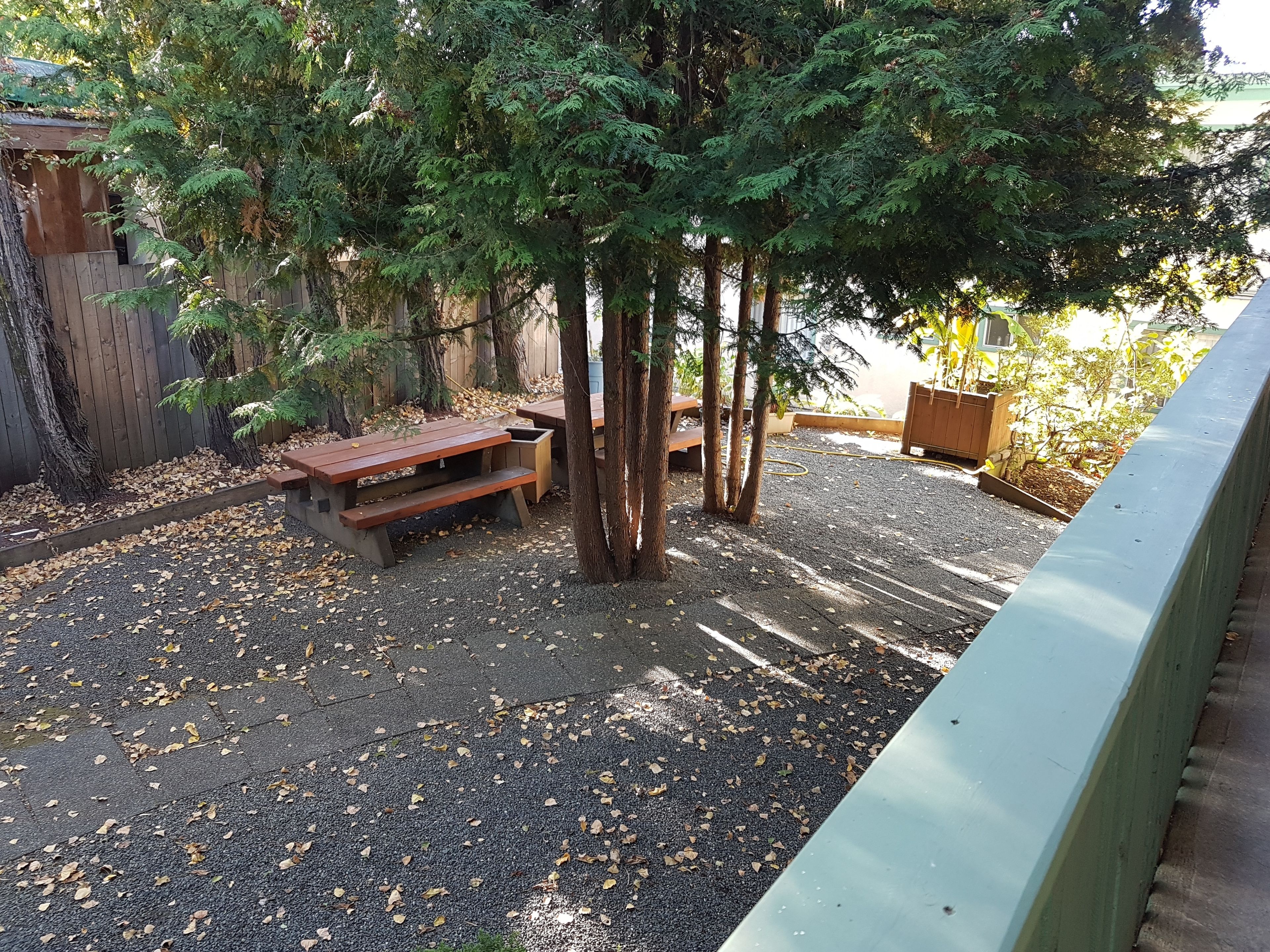A gravel patio with picnic tables and a wooden fence.