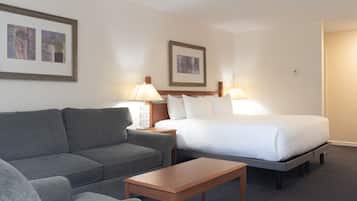 A hotel room with a grey sofa, a wooden coffee table, a bed with white linens, two bedside lamps, and two framed pictures on the wall.