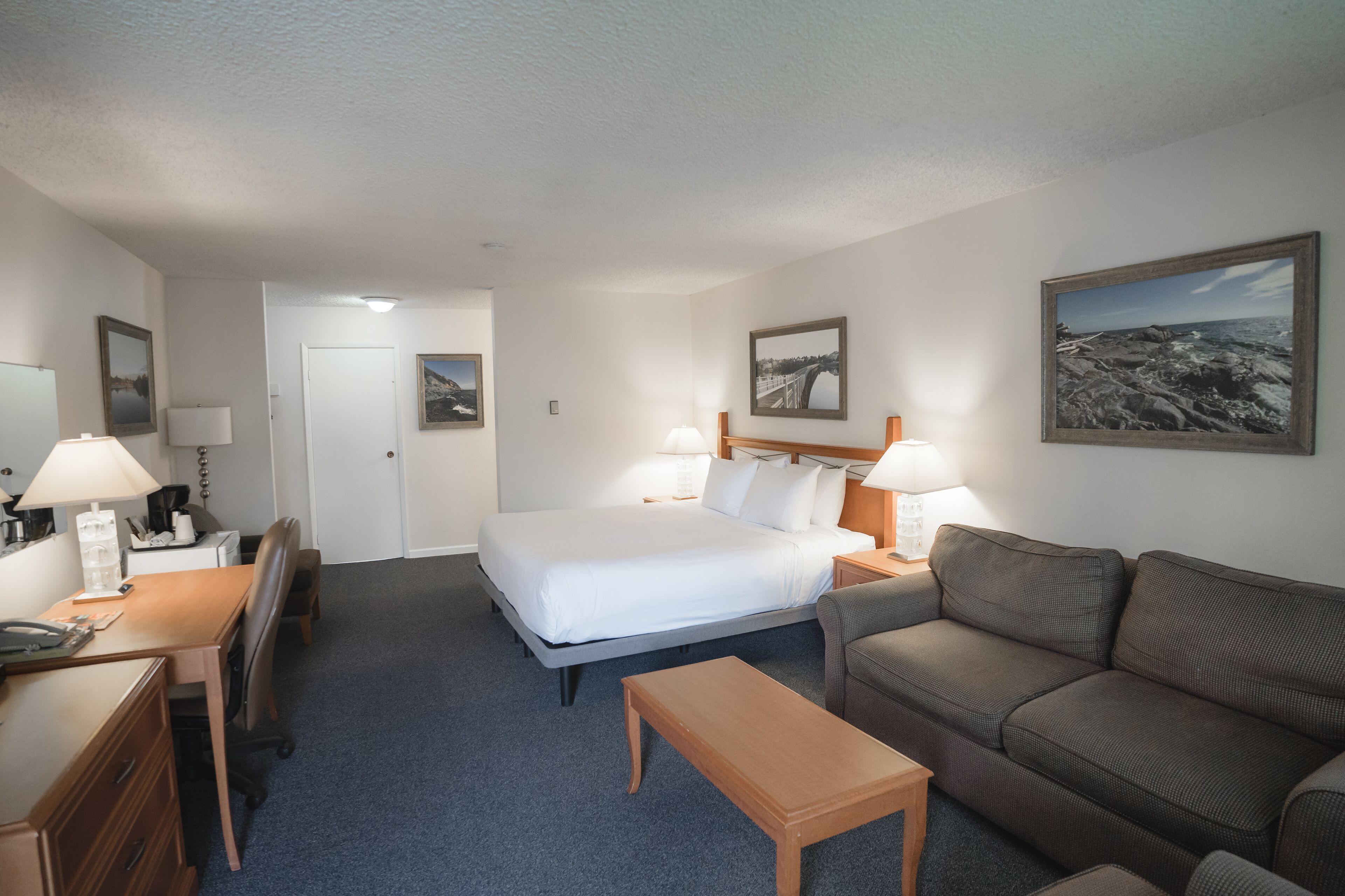 Una habitación de hotel con cama, escritorio con lámpara, sofá y dos lámparas de pared.