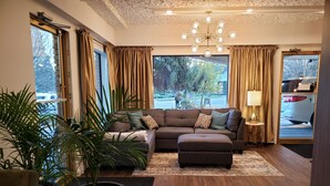 A modern living room with a sectional sofa, a large potted plant, and a view of the outdoors through large windows.