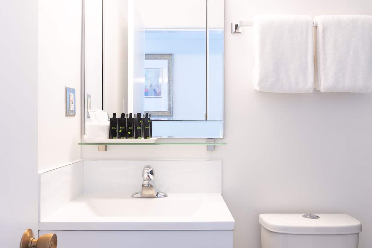 A bathroom with a white sink, a mirror, and a toilet. There are toiletries on the sink and a towel hanging on the wall.