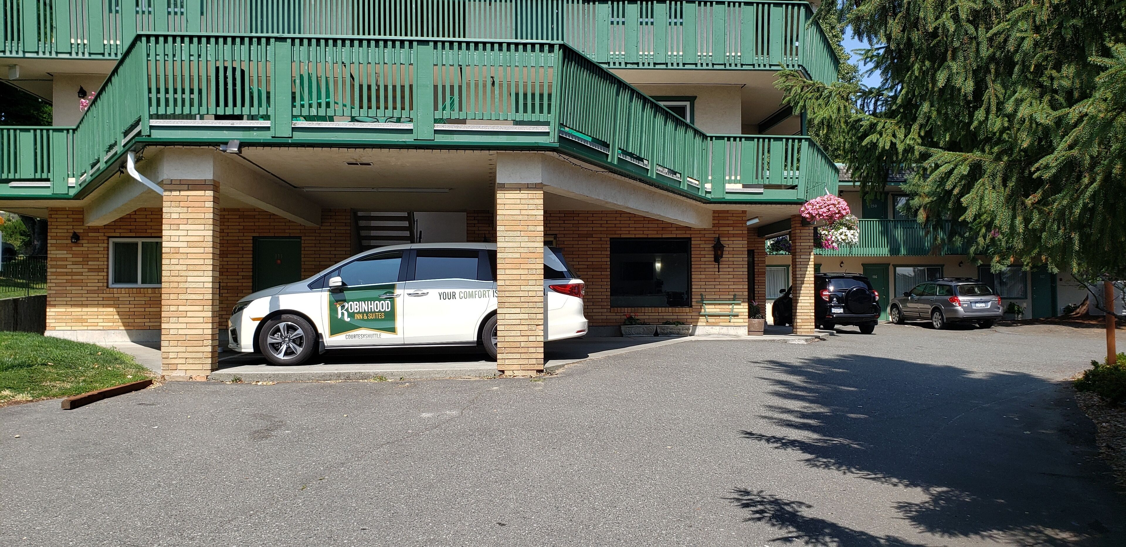 Un immeuble doté d’un balcon verdoyant et d’une voiture garée devant.