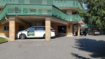 Un immeuble doté d’un balcon verdoyant et d’une voiture garée devant.