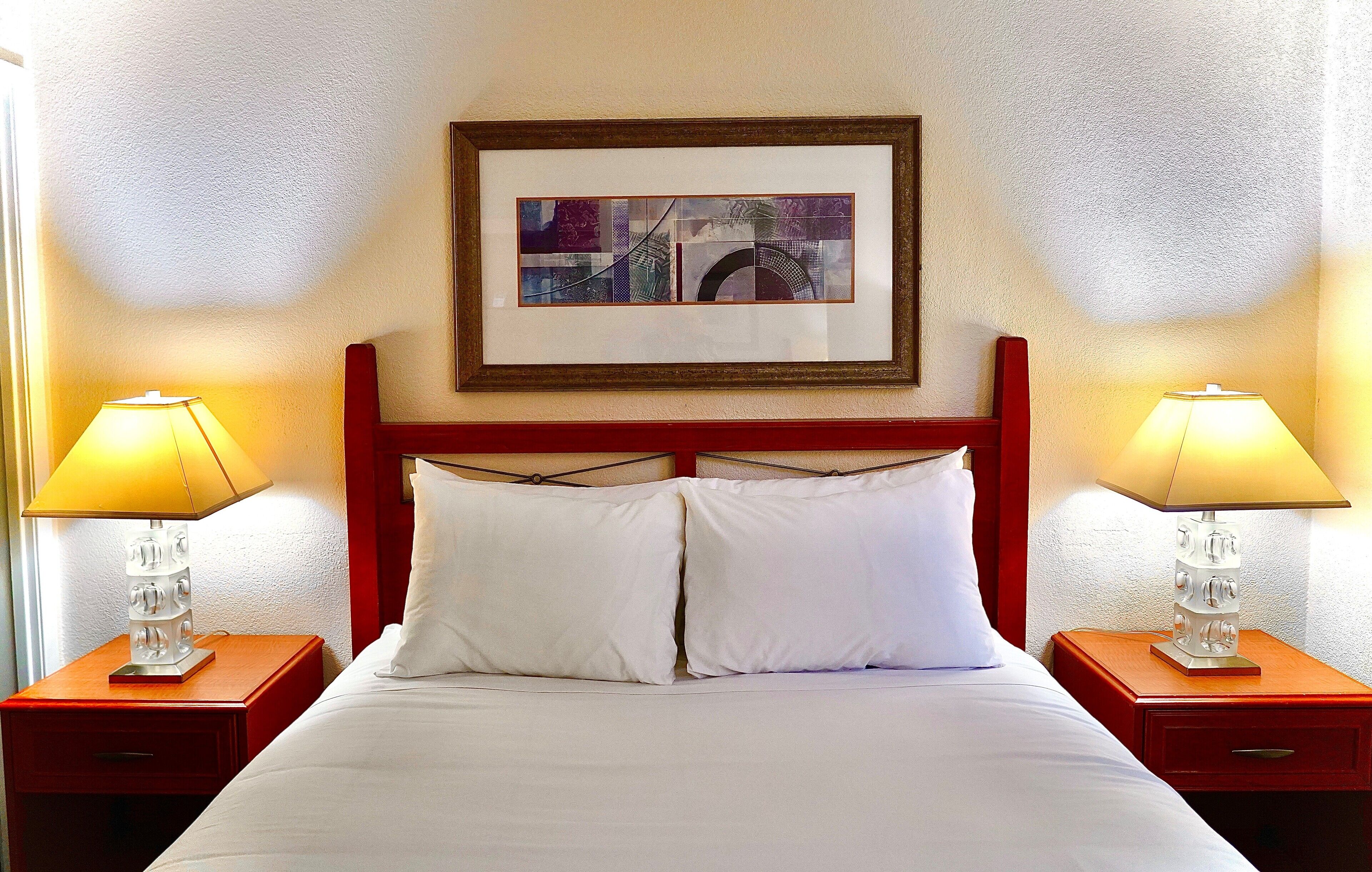 Une chambre d’hôtel avec un lit, deux tables de chevet, deux lampes et un tableau encadré au mur.