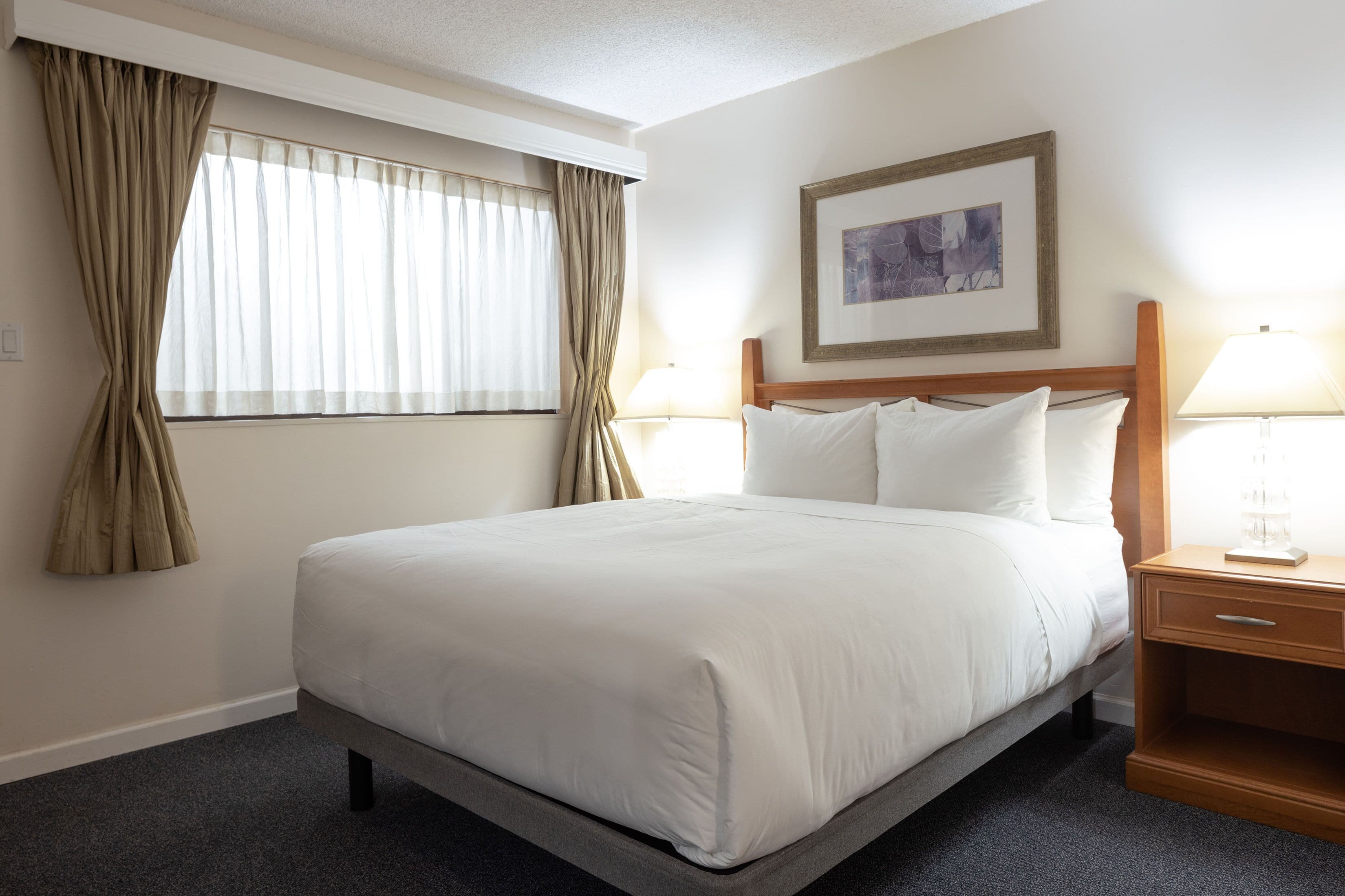A hotel room with a large bed, two bedside tables, a framed picture on the wall, and a window with curtains.