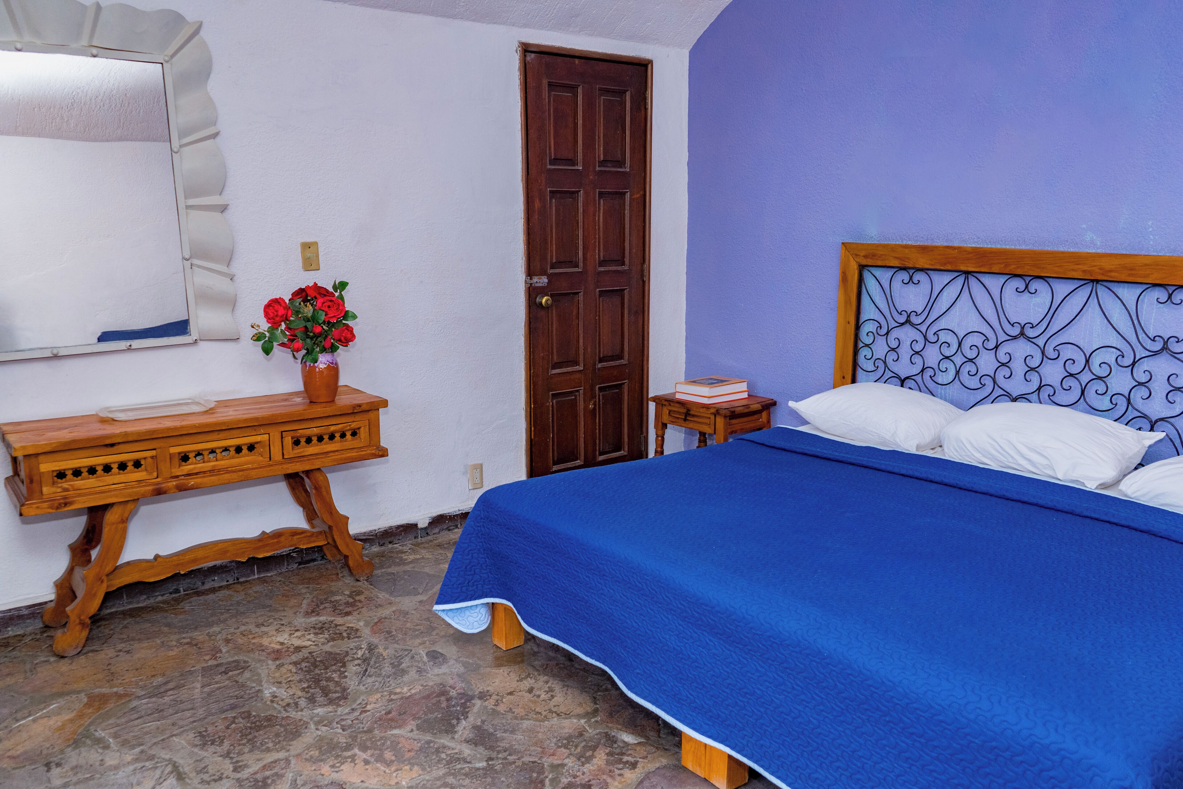 A bedroom with a bed, a wooden dresser, a mirror, and a door.