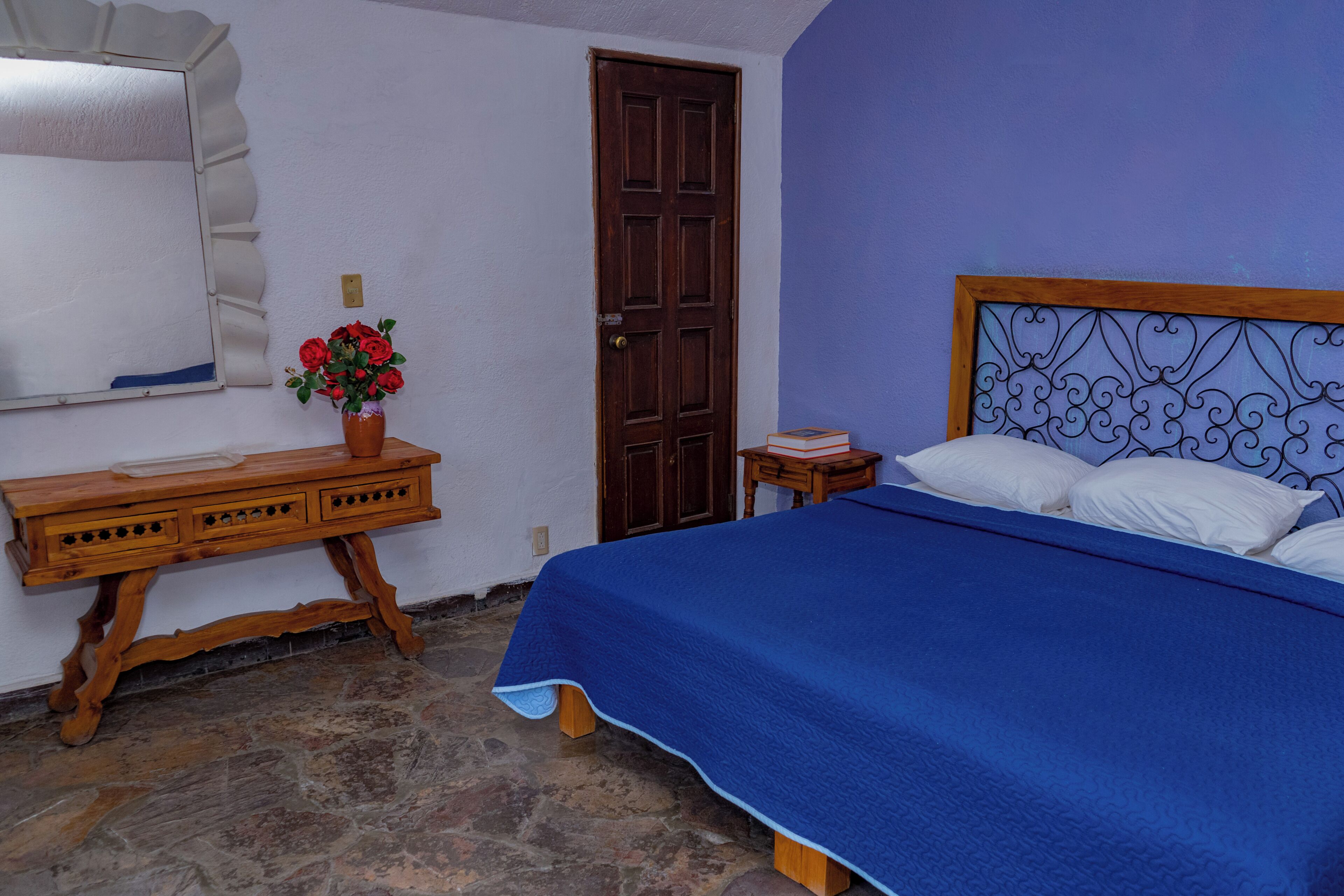 Un dormitorio con cama, cómoda de madera, espejo y puerta.