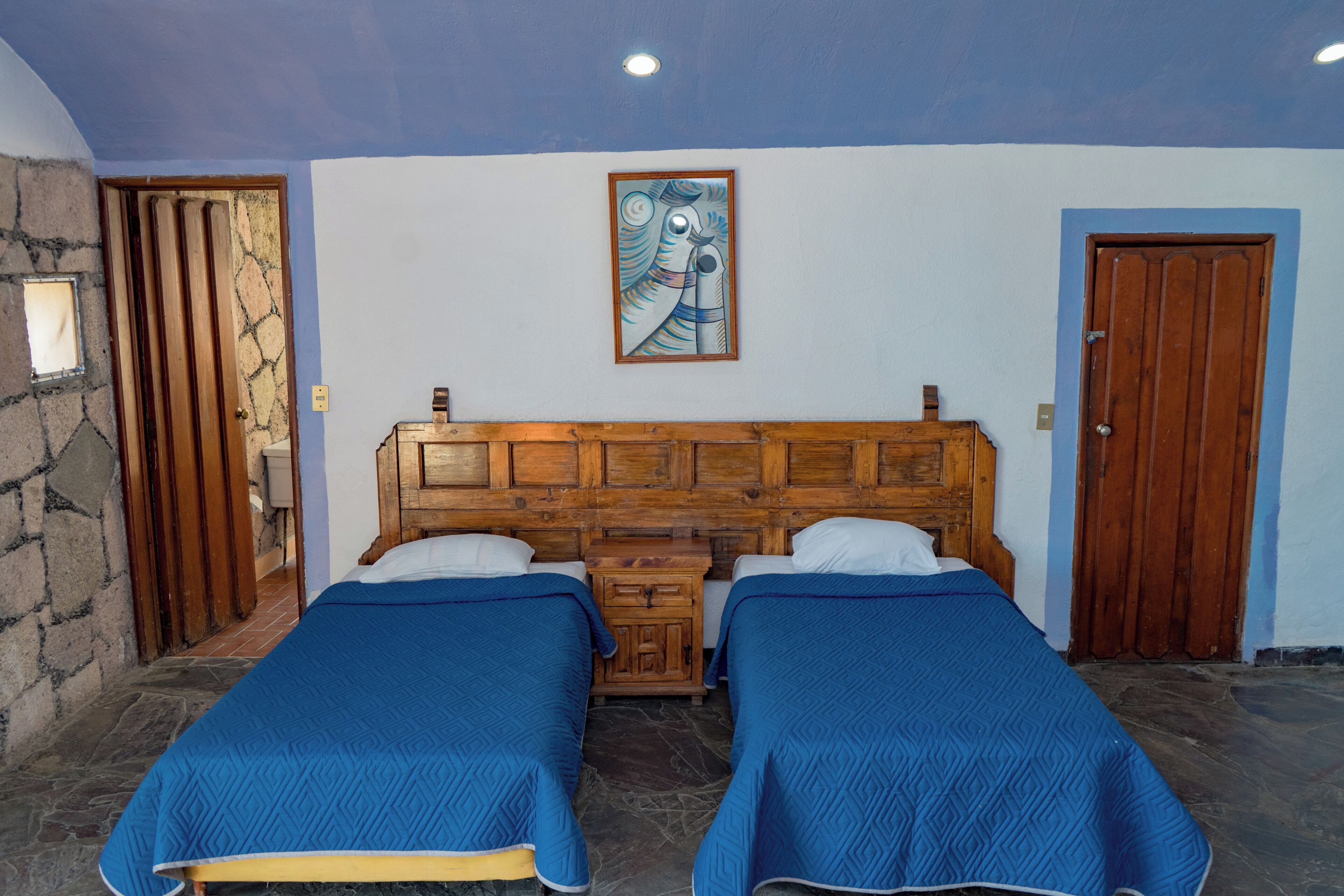 A room with two beds, a wooden headboard, a stone wall, and a wooden door.
