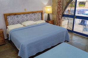 Una cama con cabecera, una lámpara de noche y vistas a una piscina al aire libre.