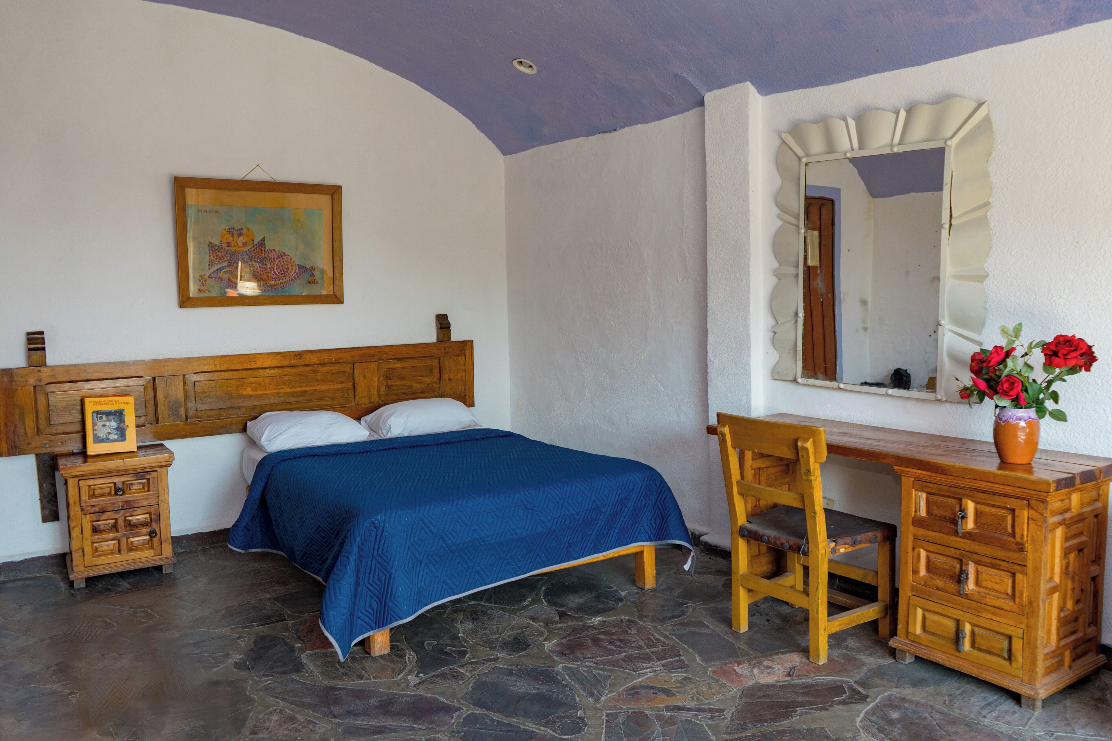Quarto com cama, cômoda de madeira, cadeira e espelho.