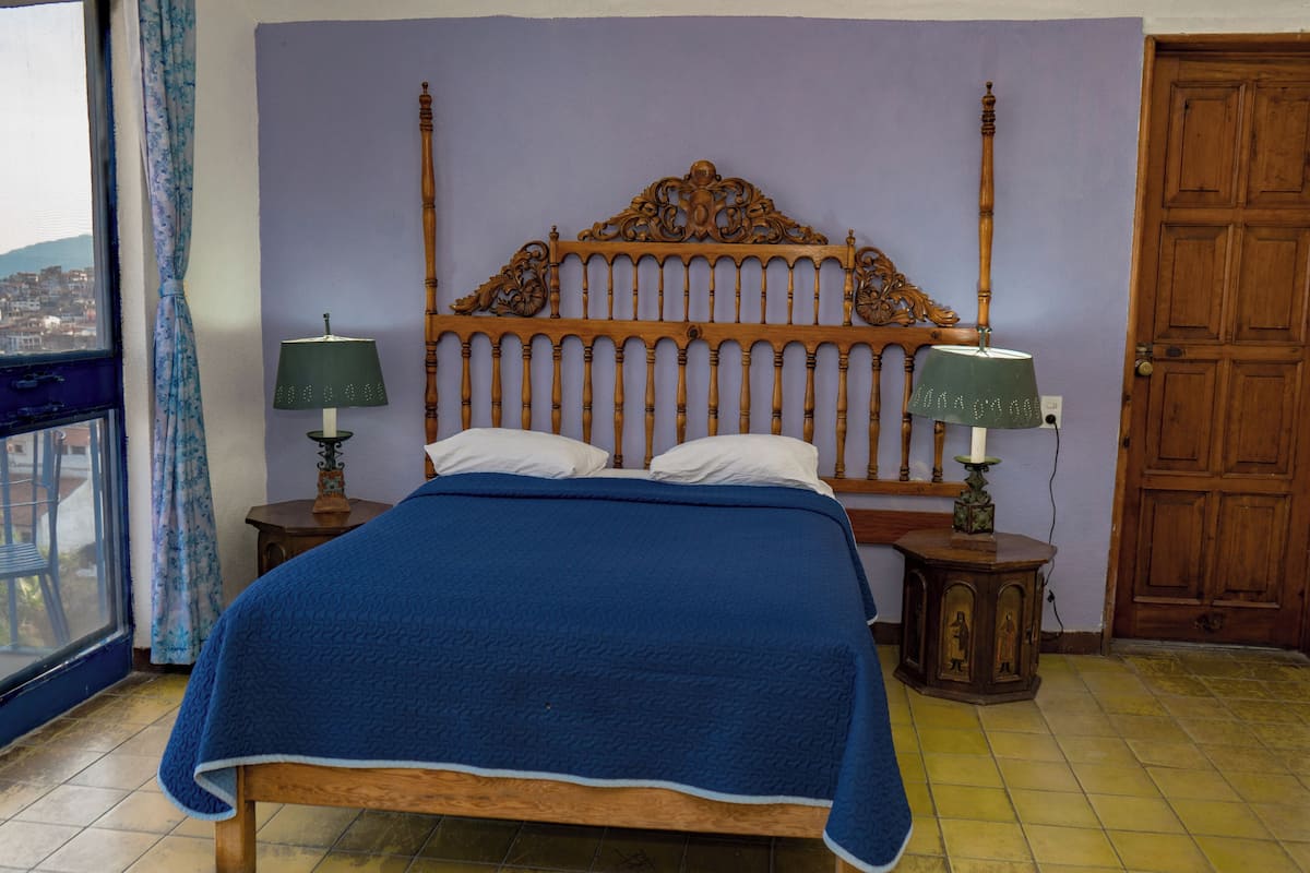 Un dormitorio con cama de madera, dos mesitas de noche, una ventana con cortinas y una puerta.